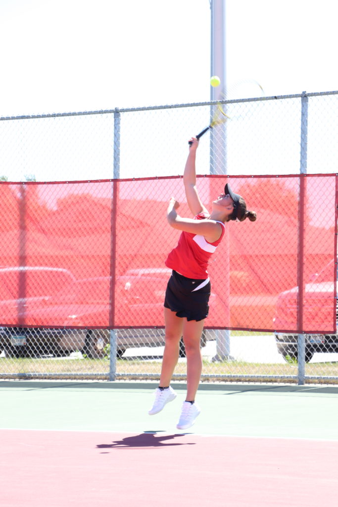 Trojan tennis player reaching up for the ball