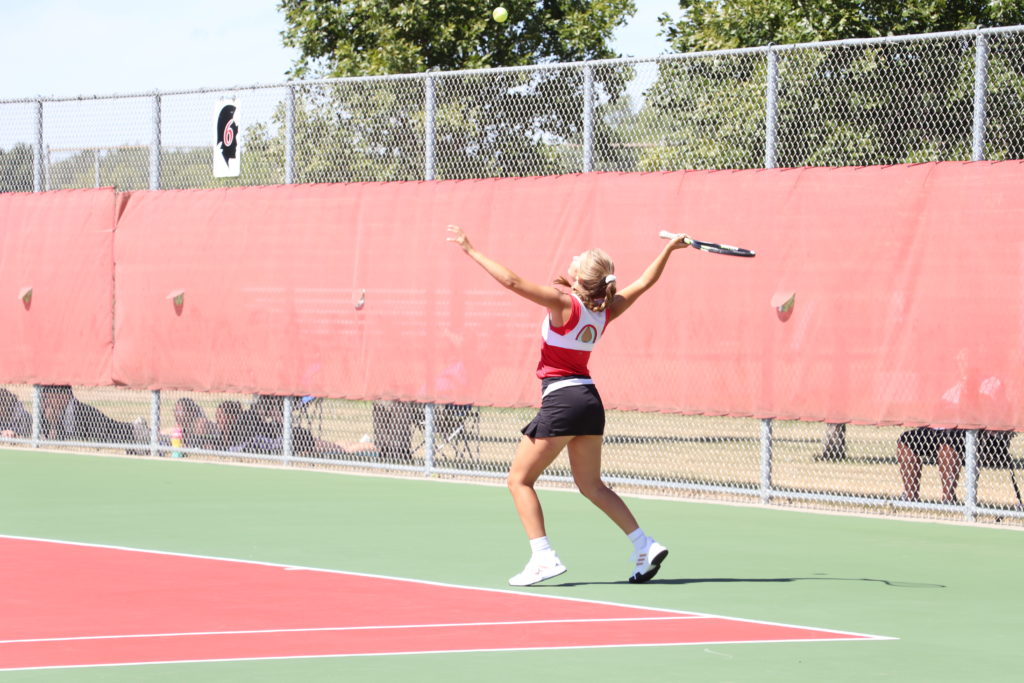 Trojan tennis player reaching up for the ball