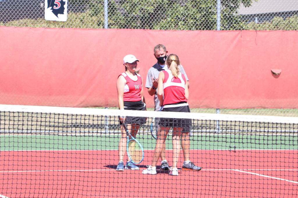 Two Trojan tennis players conferring with the coach