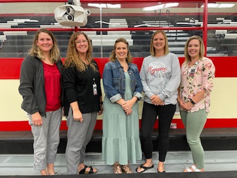 Jen Brands, Shanelle Henning, Wendy Donkersloot, Kayla Schmitz, Jackie Heidelberger standing in front of the bleachers.