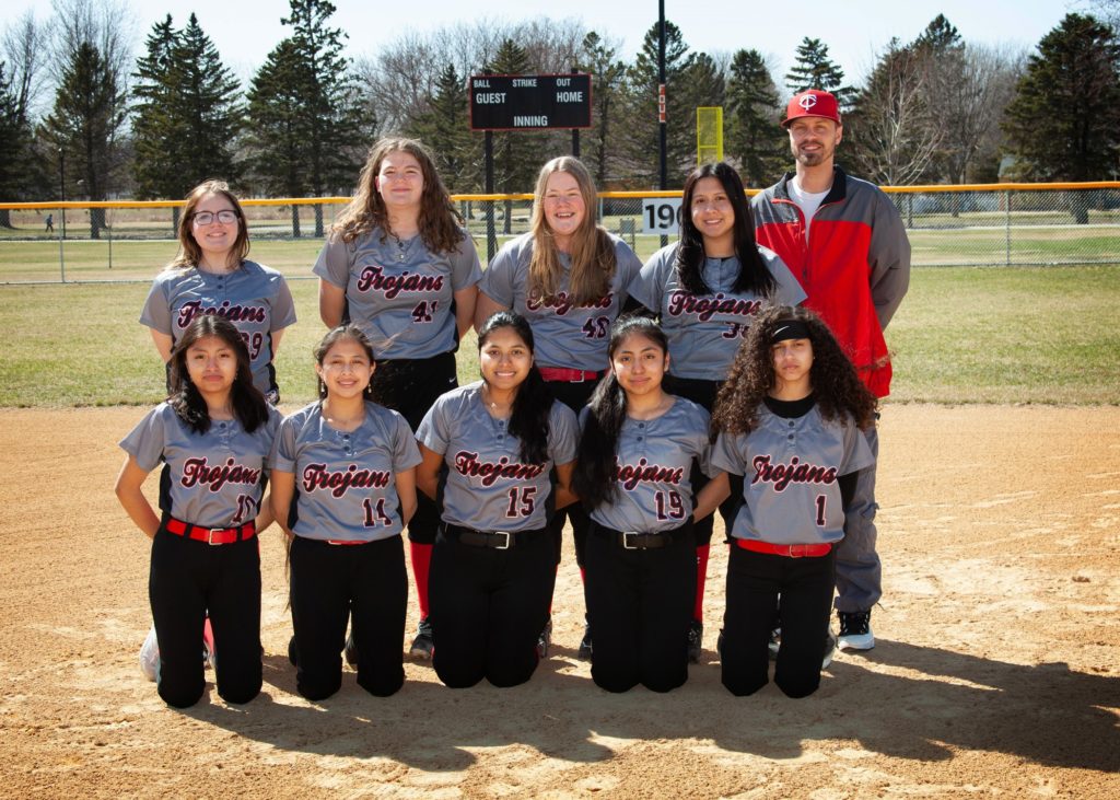 Nine girls in uniform on the softball field with the coach