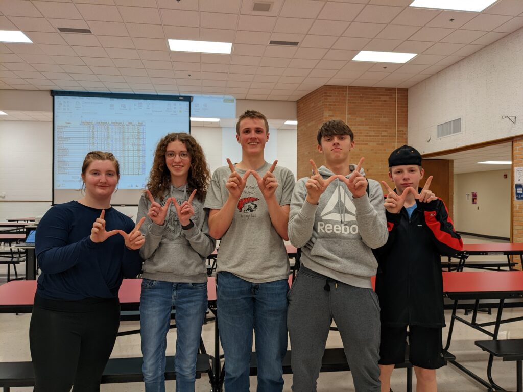 Five students making W's with their fingers in the cafeteria