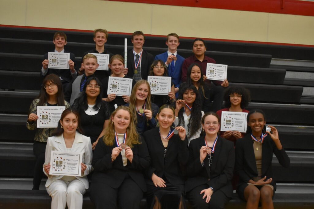 19 students in 4 rows on the bleachers showing certificates and medals