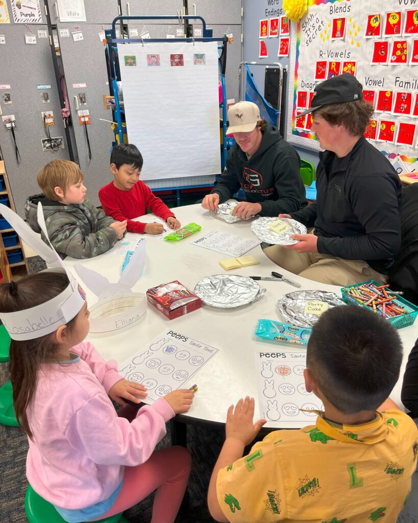 2 high school students at a table with elementary students doing Peeps activity