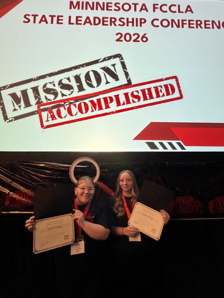 two students in front of Mission Accomplished sign holding certificates