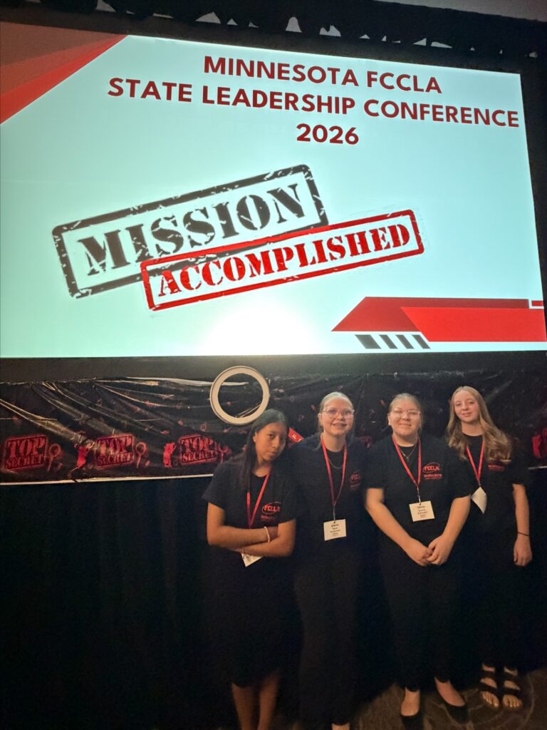 four student standing in front of Mission Accomplished sign 
