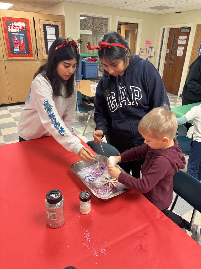 2 students helping a preschooler with an art project